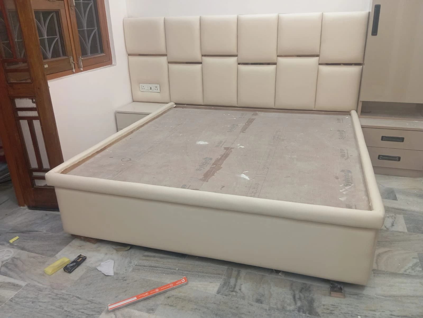 Custom cream upholstered king-size bed with padded headboard being installed at customer home in Lucknow by Prajapati Electrical