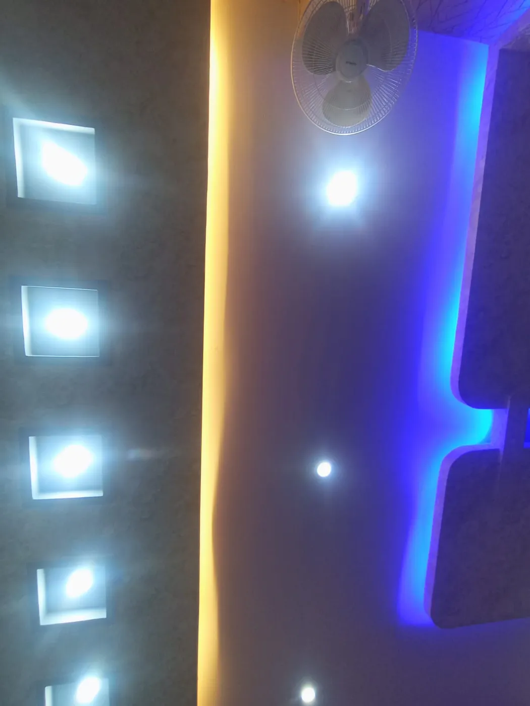 False ceiling with a row of square LED spot lights, blue cove lighting and ceiling fan in Lucknow by Prajapati Electrical